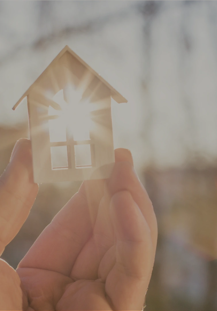 An image showing a hand holding a miniature of a home with sun rays shining through it.